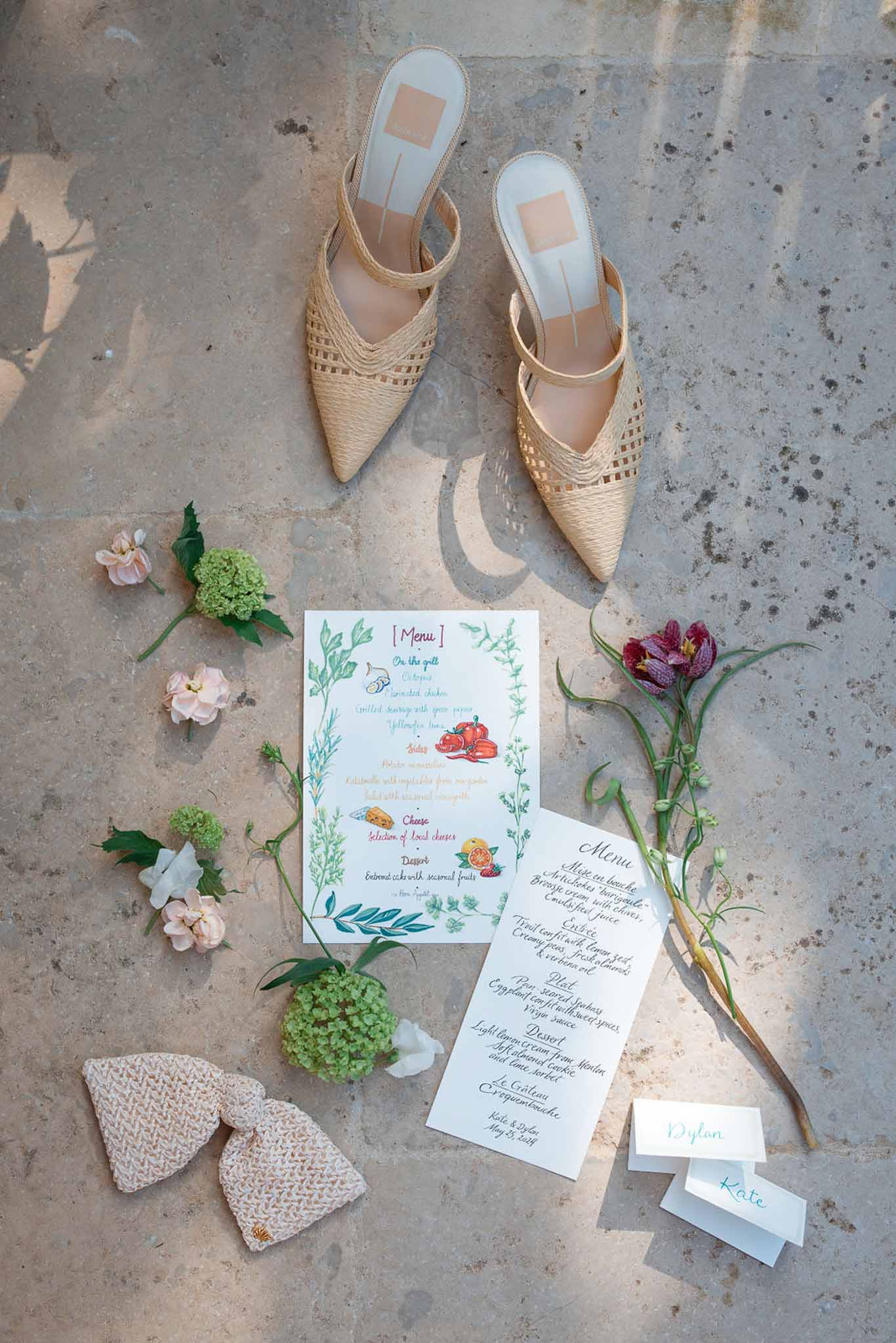 Wedding flat lay with bride's shoes, menu cards, and floral arrangements on concrete surface