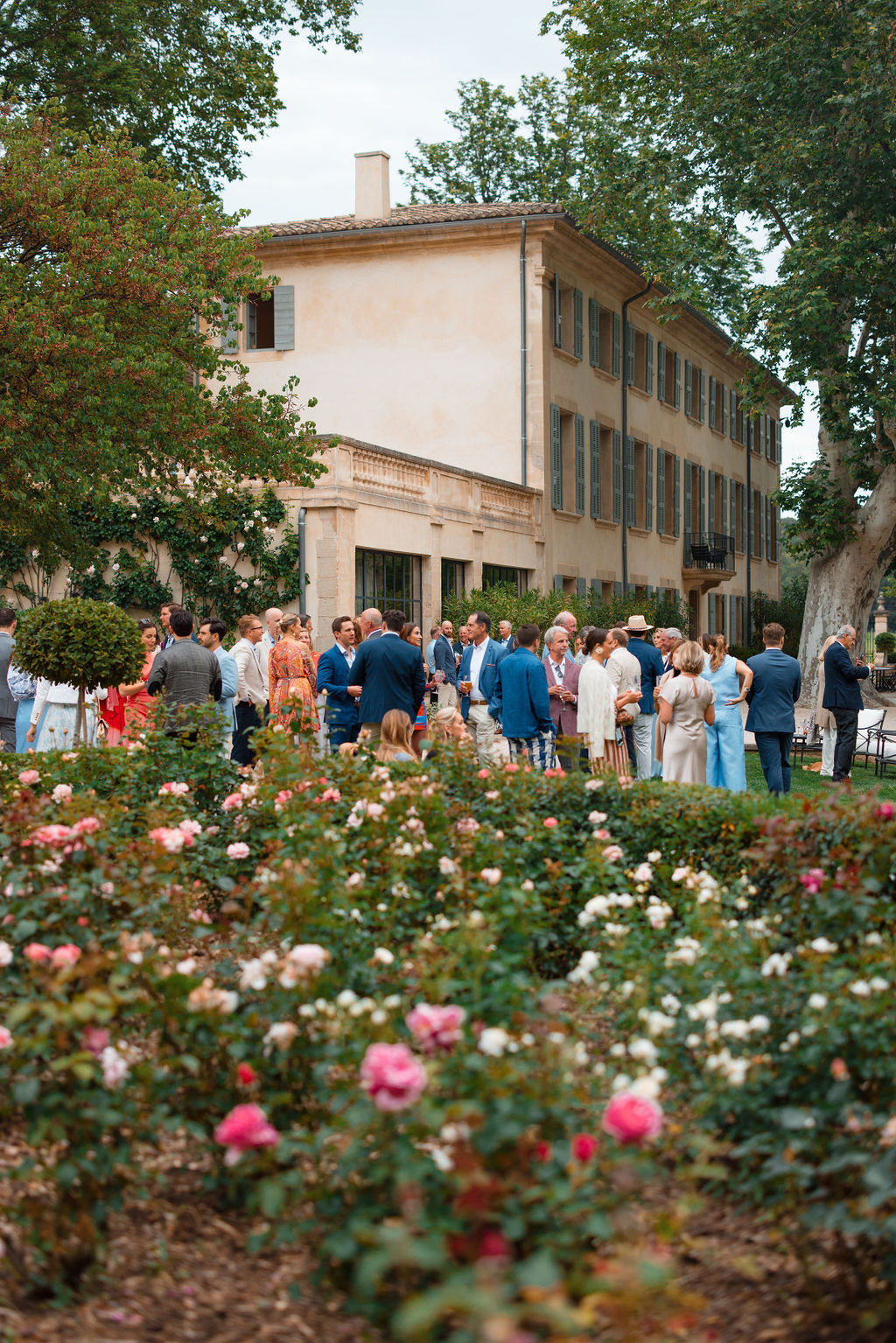 Cocktail hour gathering in manicured gardens at historic Tuscan villa with blooming roses
