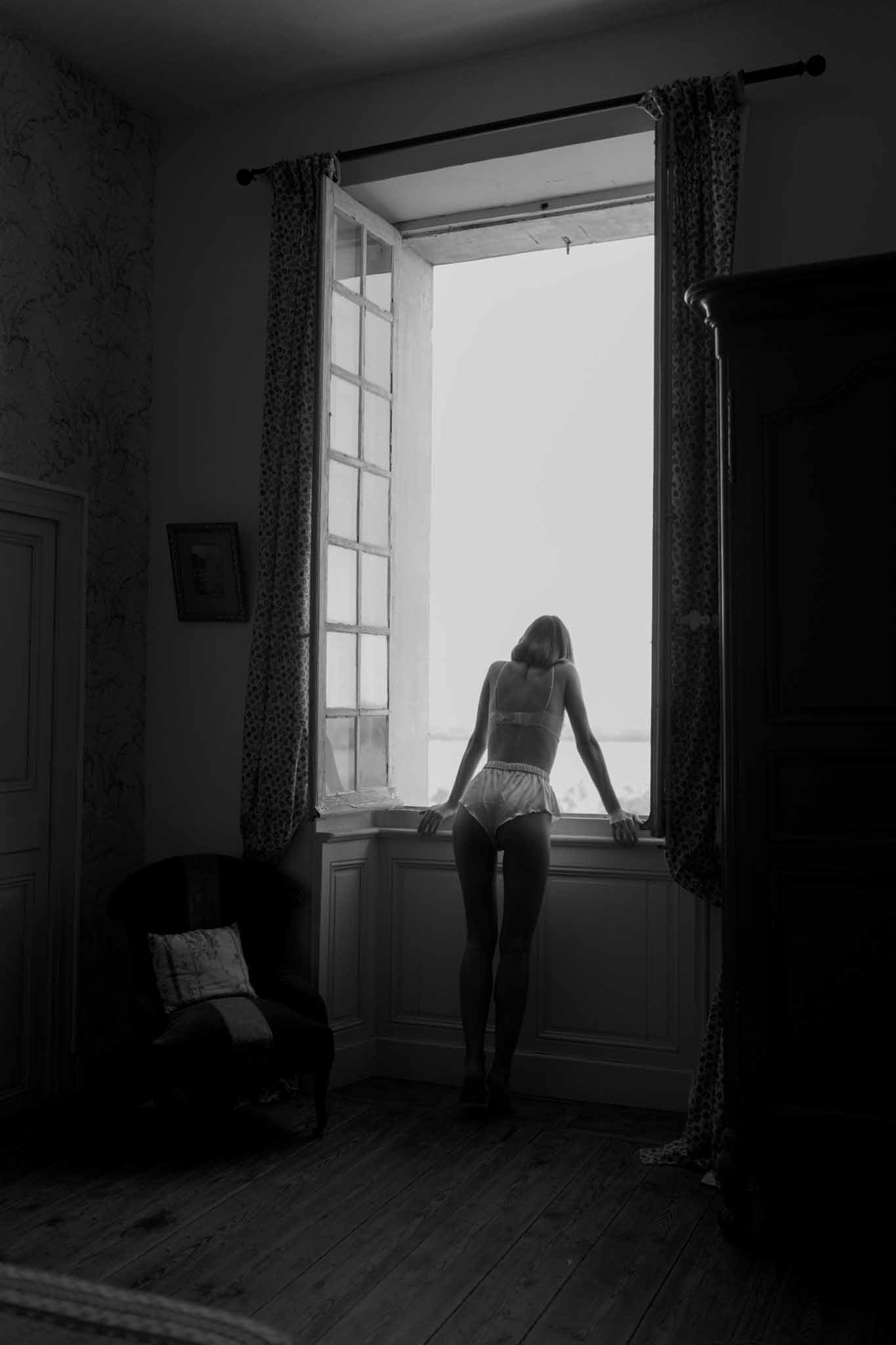 Black and white bride in lingerie looking out window during getting-ready moment