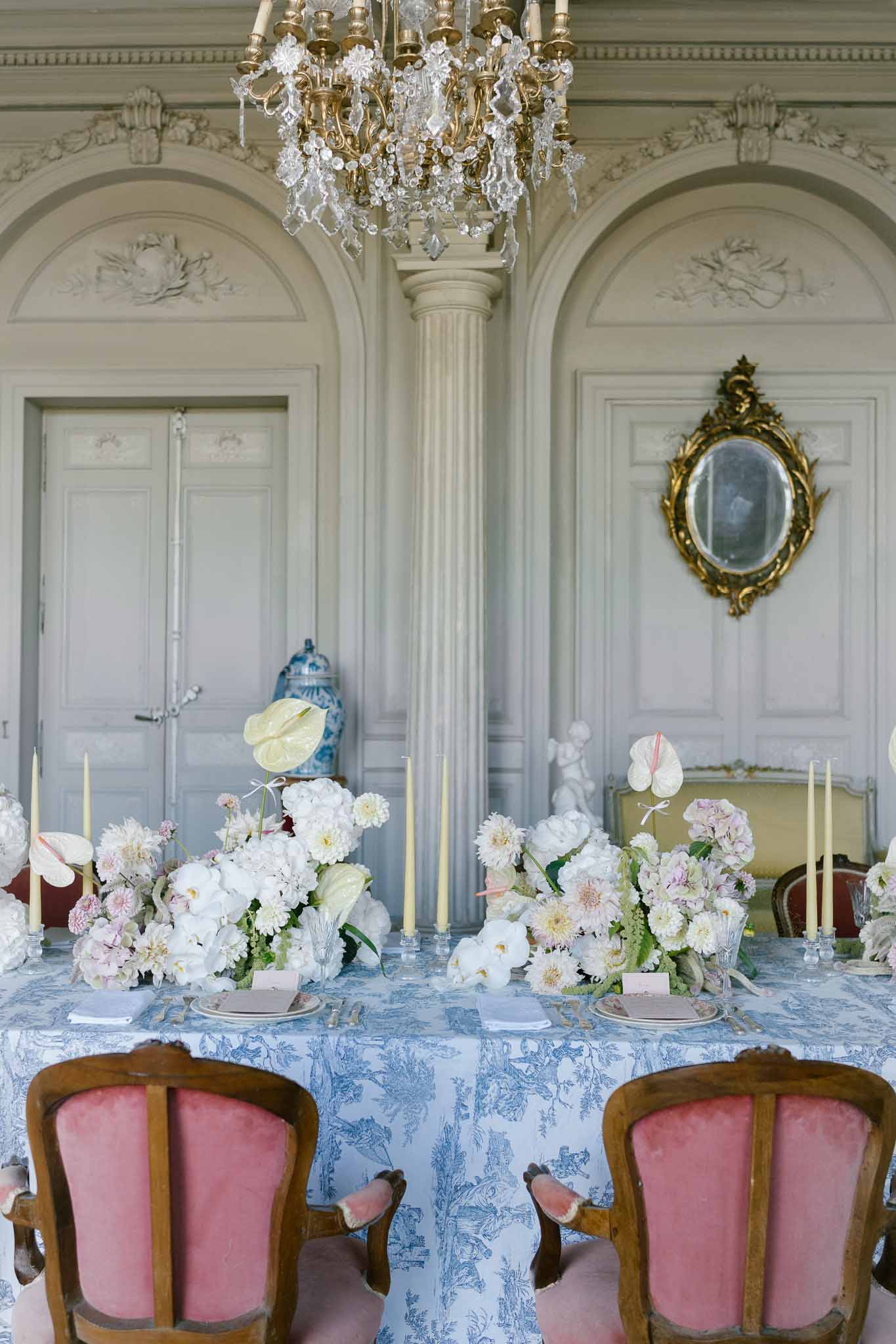 Chateau salon reception with blue toile linen white peony centerpieces dusty rose velvet chairs and grey boiserie panels