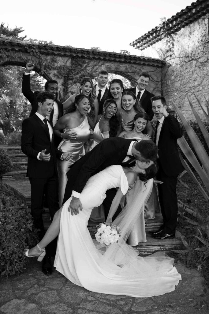 manoir de letang myrto events bride groom dip kiss entourage cheering back black white photo