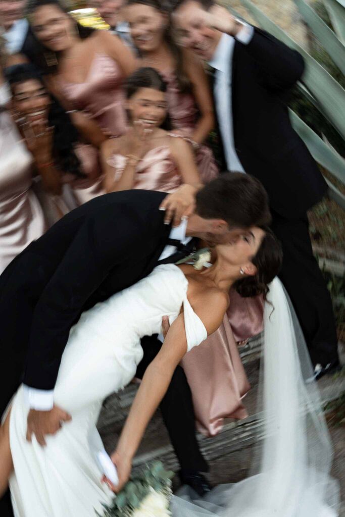 manoir de letang myrto events bride groom dip kiss entourage cheering back blurry