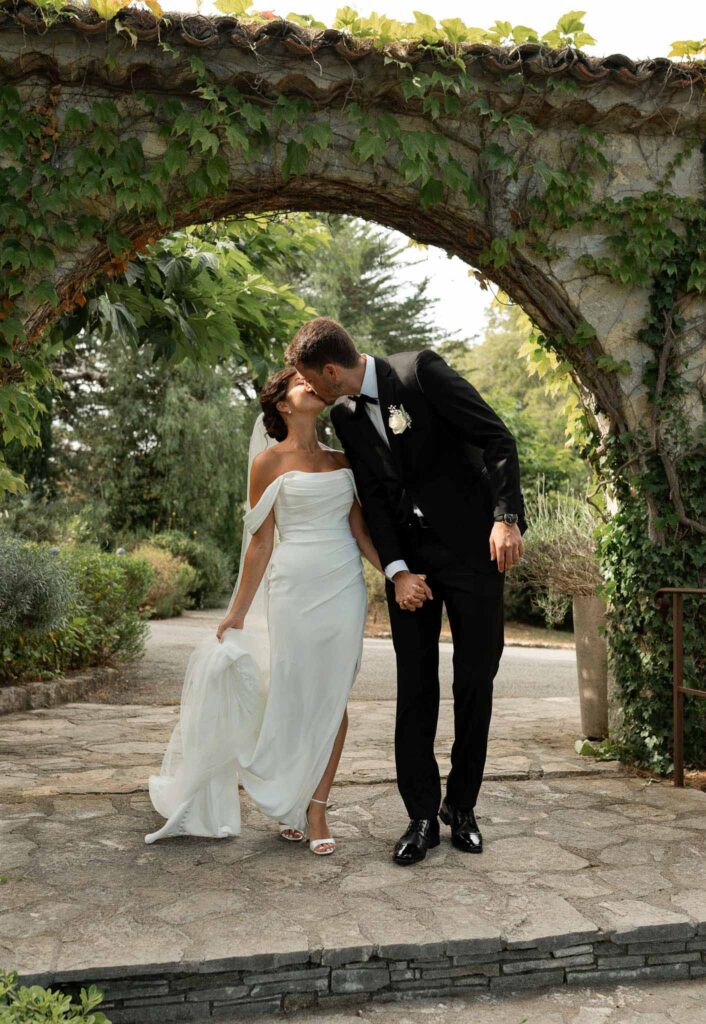 manoir de letang myrto events groom bride holding hands walking kissing stone arch background