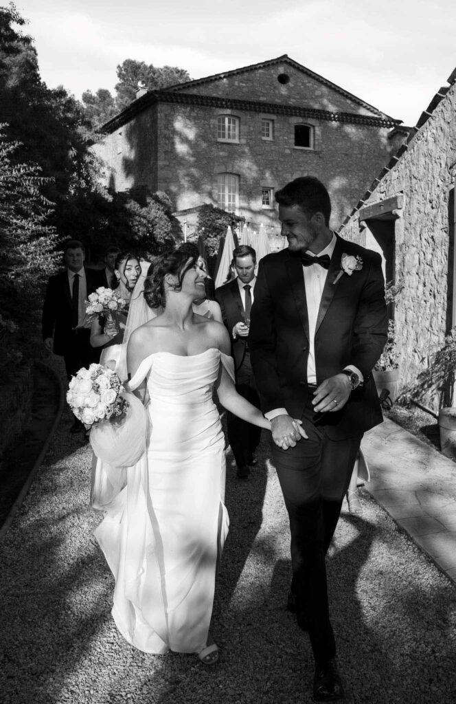 manoir de letang myrto events groom bride walking entourage at the back black white photo