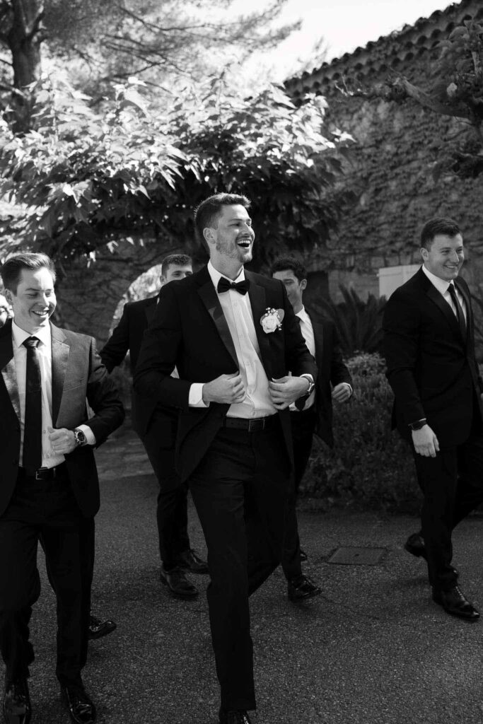 manoir de letang myrto events groom groomsmen walking holding tuxedo black white photo