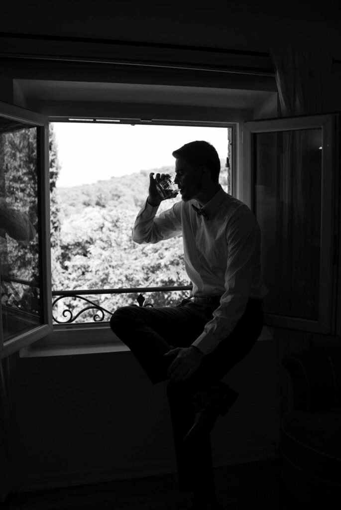 manoir de letang myrto events groom sitting by the window drinking black white photo getting ready