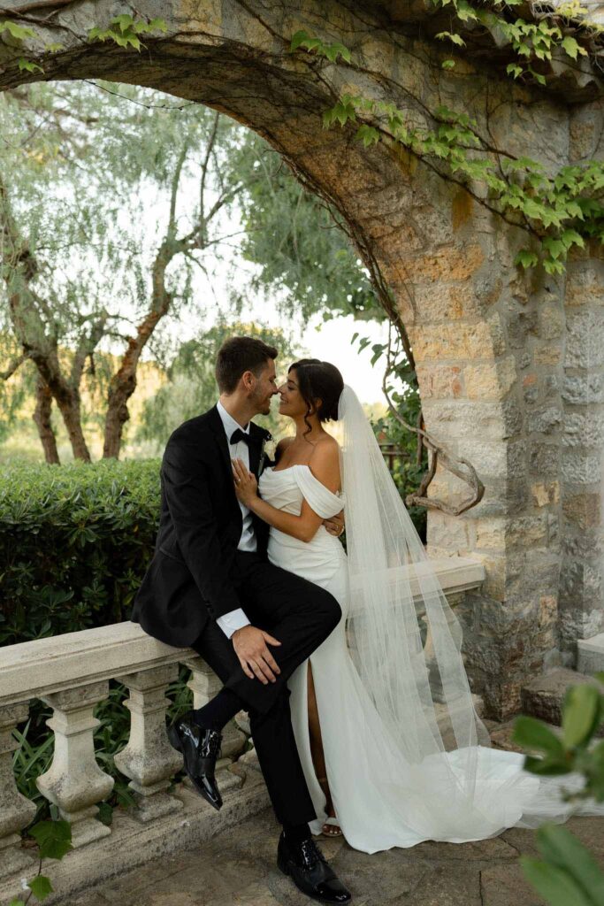 manoir de letang myrto events groom sitting vintage stone ledge hugging bride garden area
