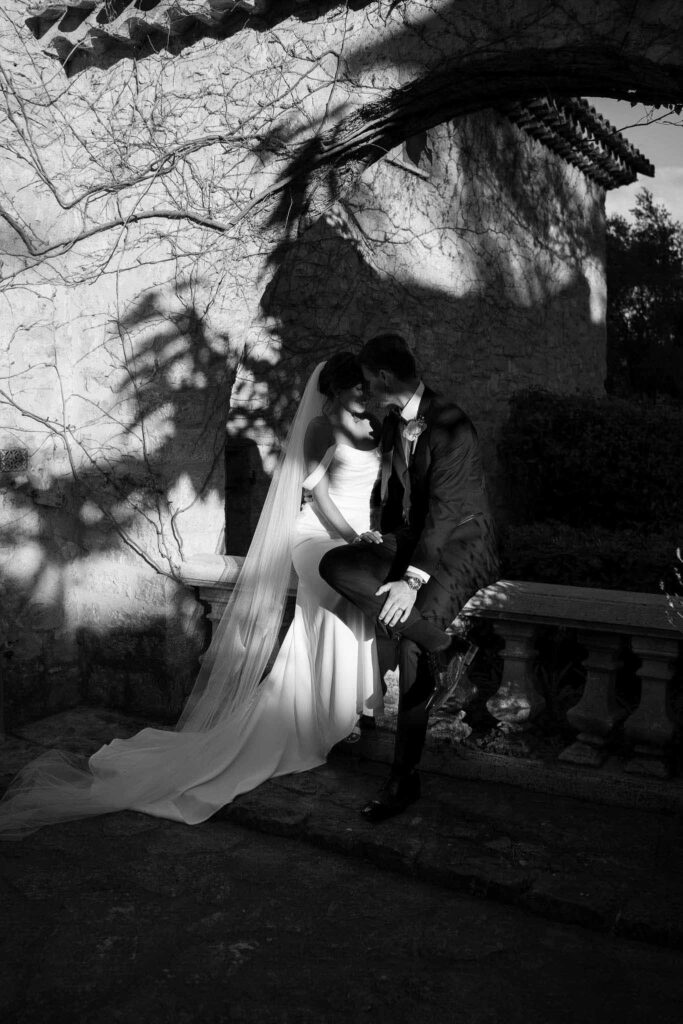 manoir de letang myrto events groom sitting vintage stone ledge hugging bride garden area black white photo