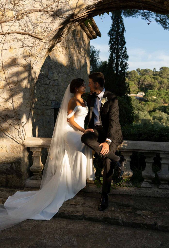 manoir de letang myrto events groom sitting vintage stone ledge hugging bride garden area sunset