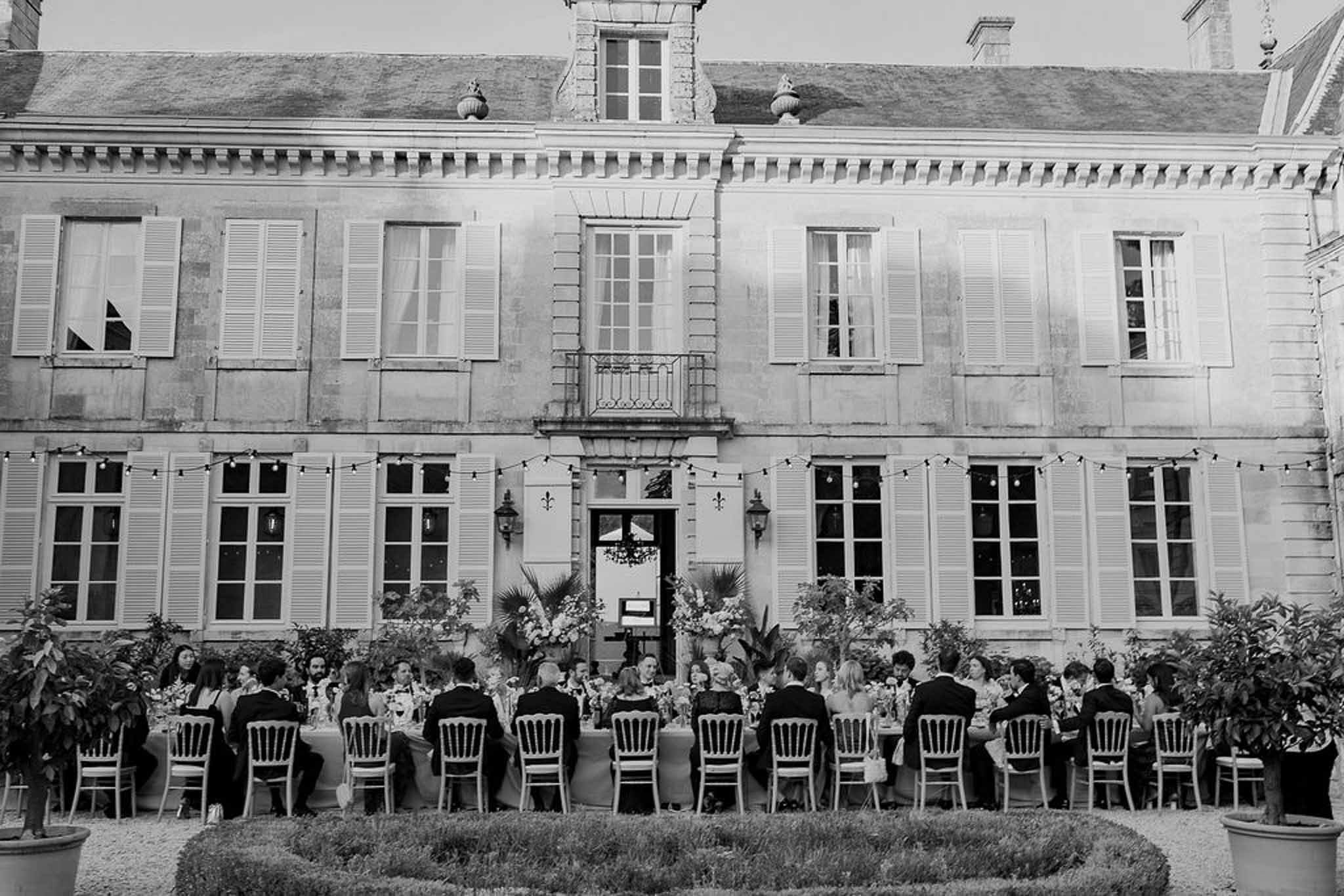 Black and white aerial banquet dinner with string lights and Chiavari chairs against chateau facade