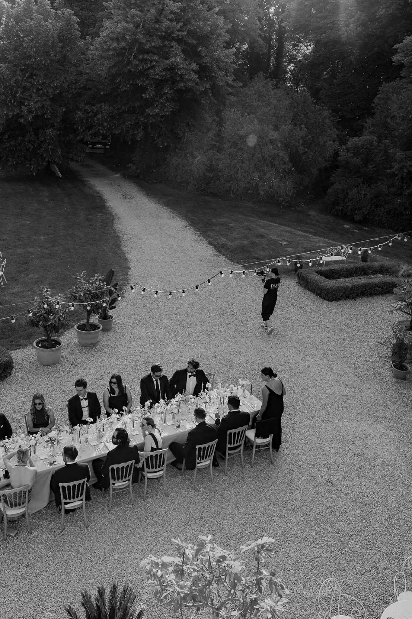 Black and white aerial view of formal dinner table with candles and guests on chateau courtyard
