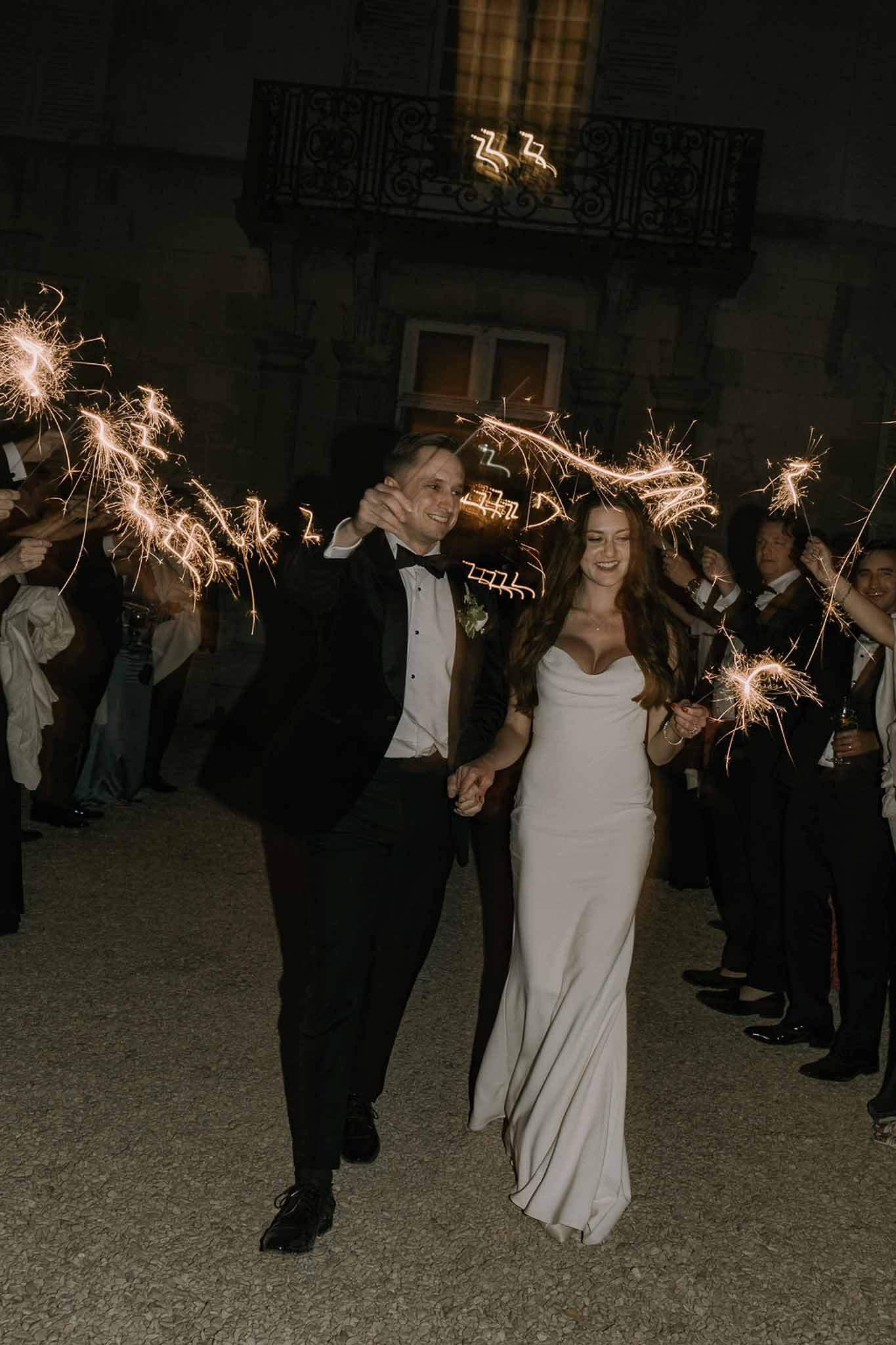 Bride and groom sparkler exit at night walking through guest tunnel at a French chateau courtyard