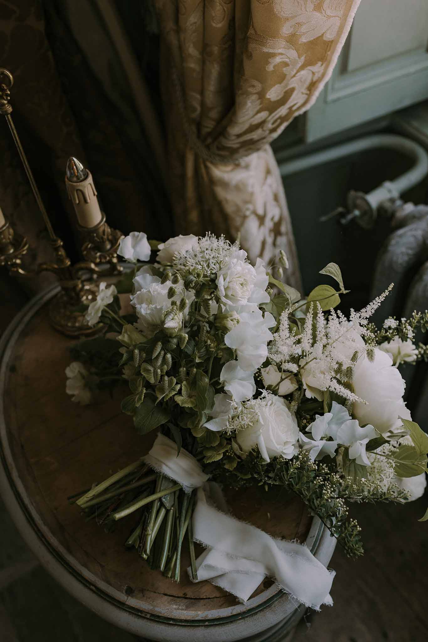 White peony and garden rose bridal bouquet with silk ribbon on antique side table