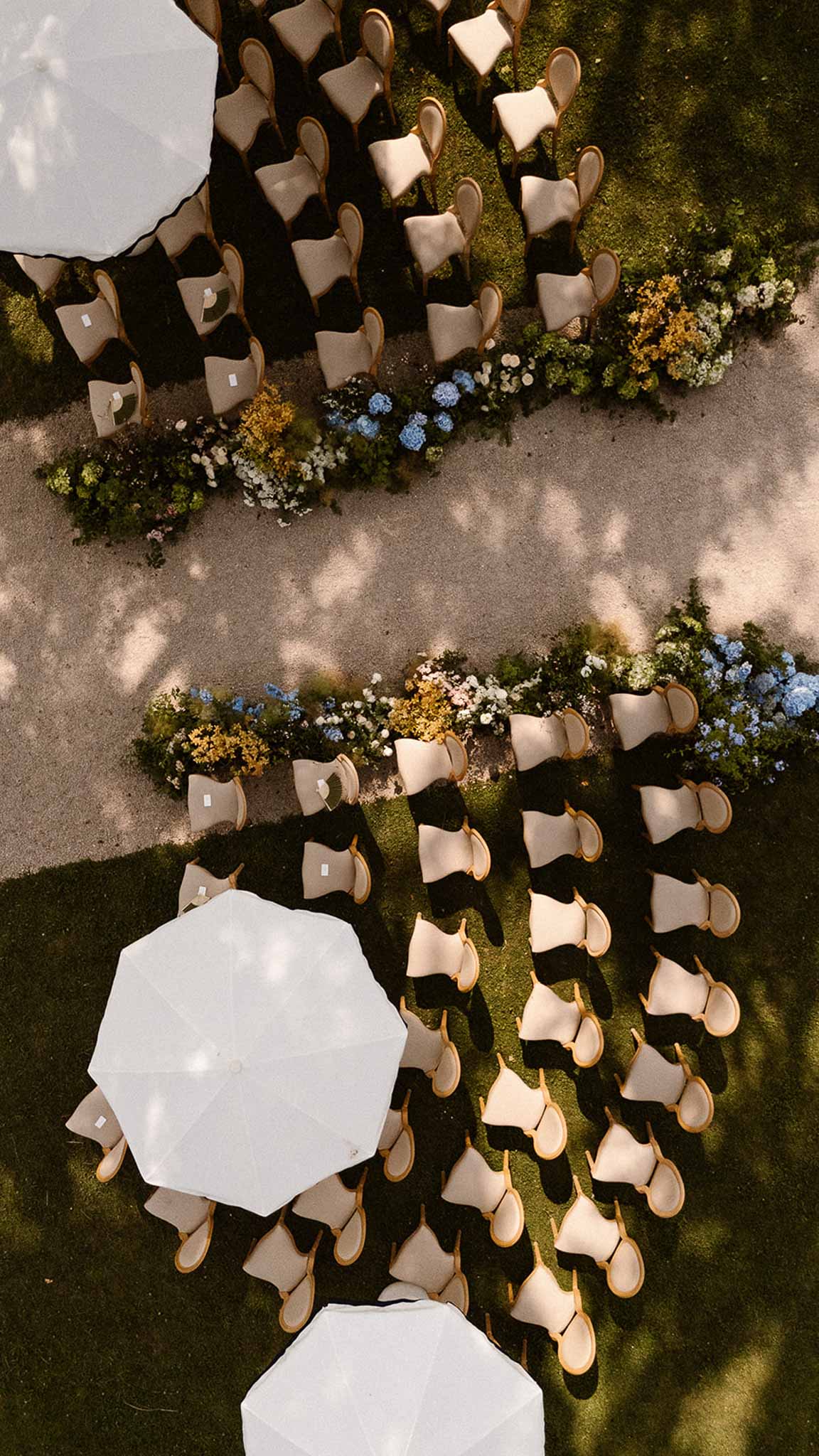 Aerial view of curved ceremony seating with blue hydrangea and yellow aisle florals and white umbrellas