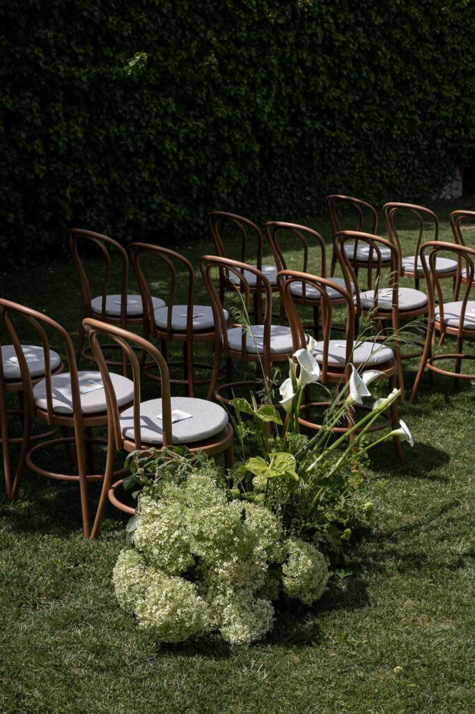 MCaelicia Galinier Lourmarin detail shot long ceremony wood chairs garden flower arrangement