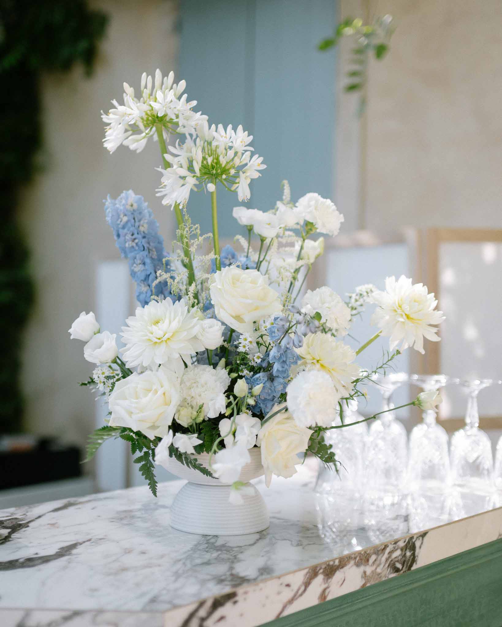 White and blue floral arrangement of agapanthus and roses in ceramic urn at marble bar counter