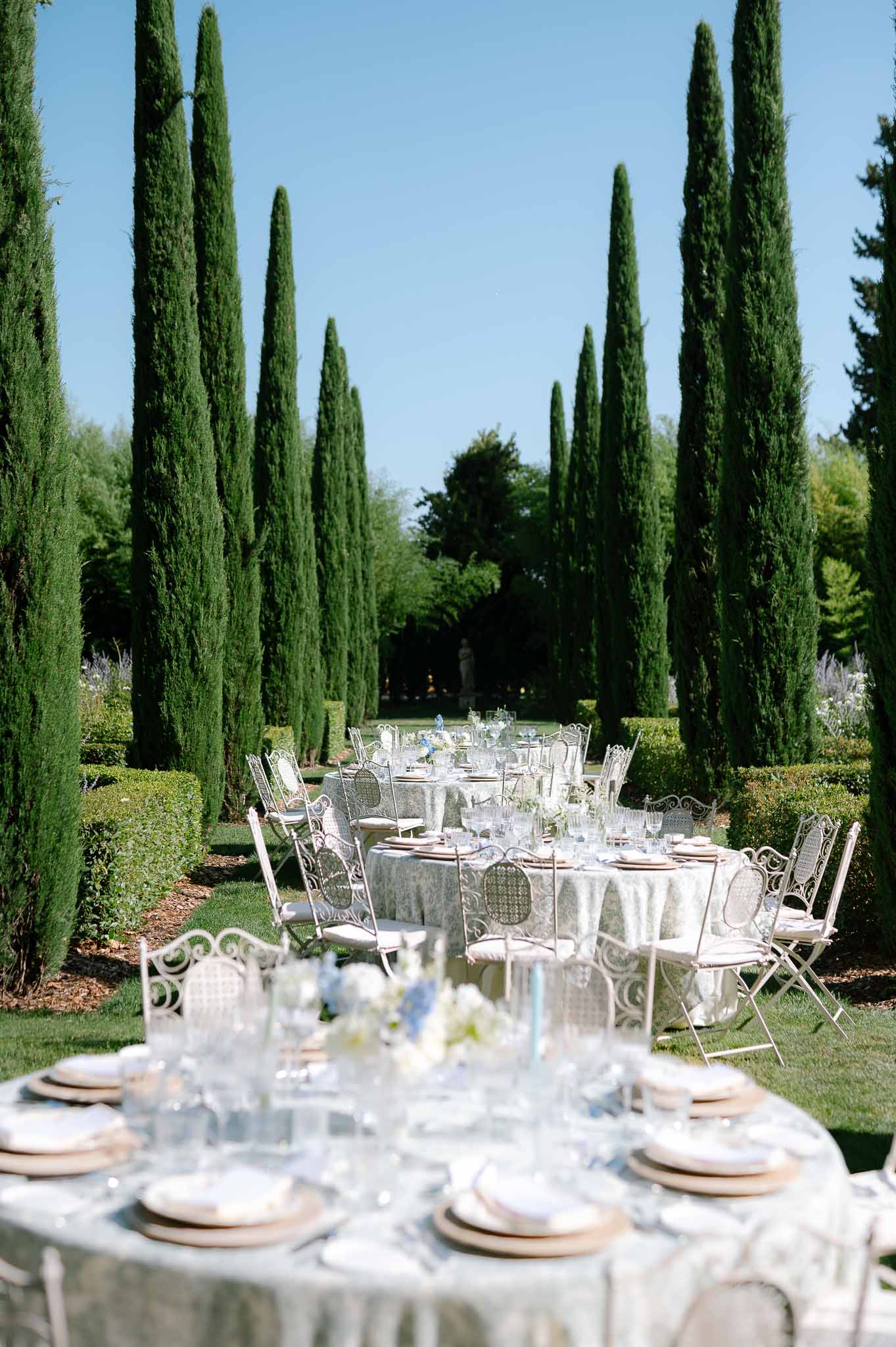 Round tables in sage linen with white hydrangea and delphinium centerpieces in cypress-lined garden