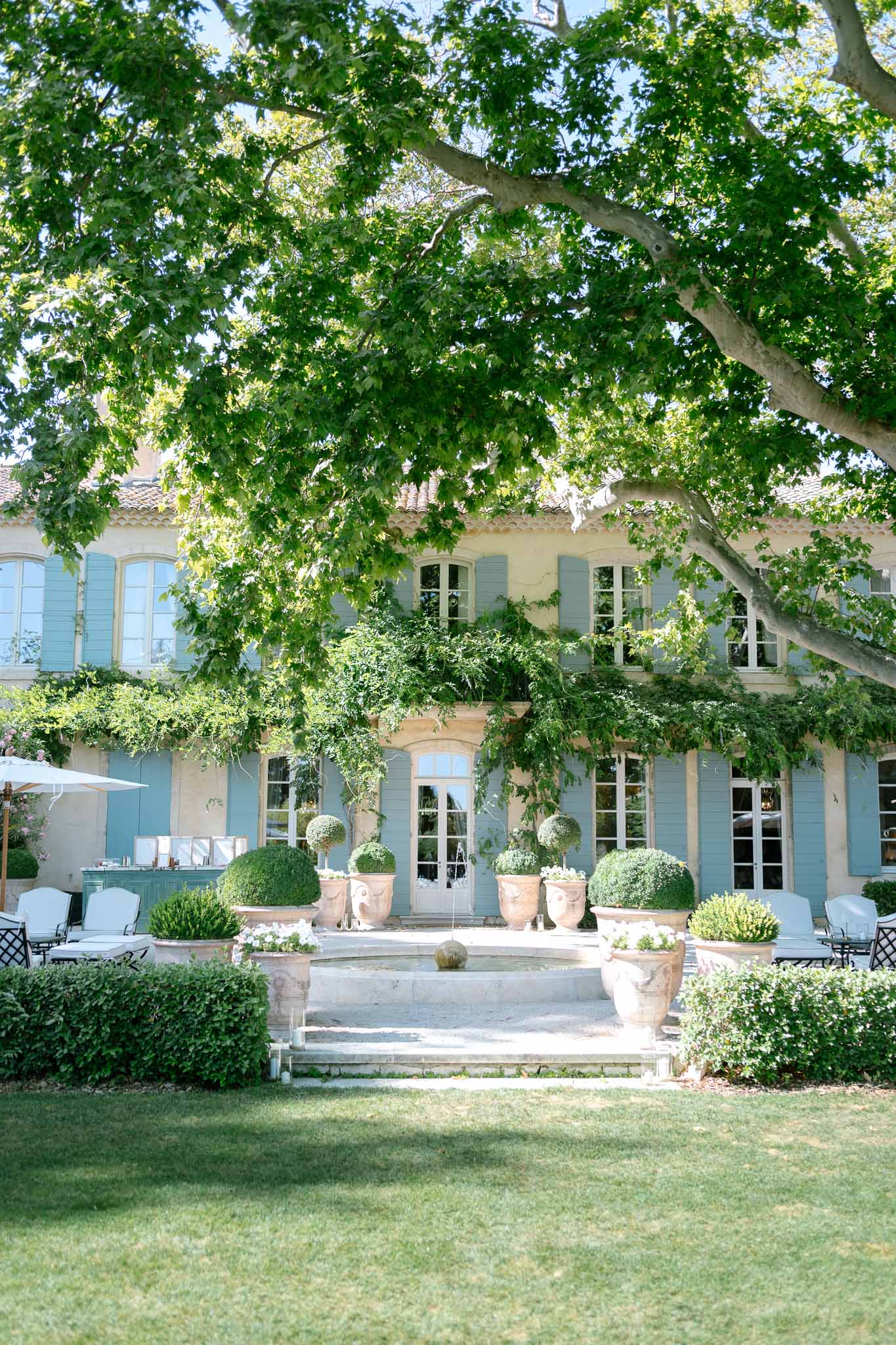 Provencal manor house with ochre walls, blue shutters, and topiary-lined terrace with lounge seating