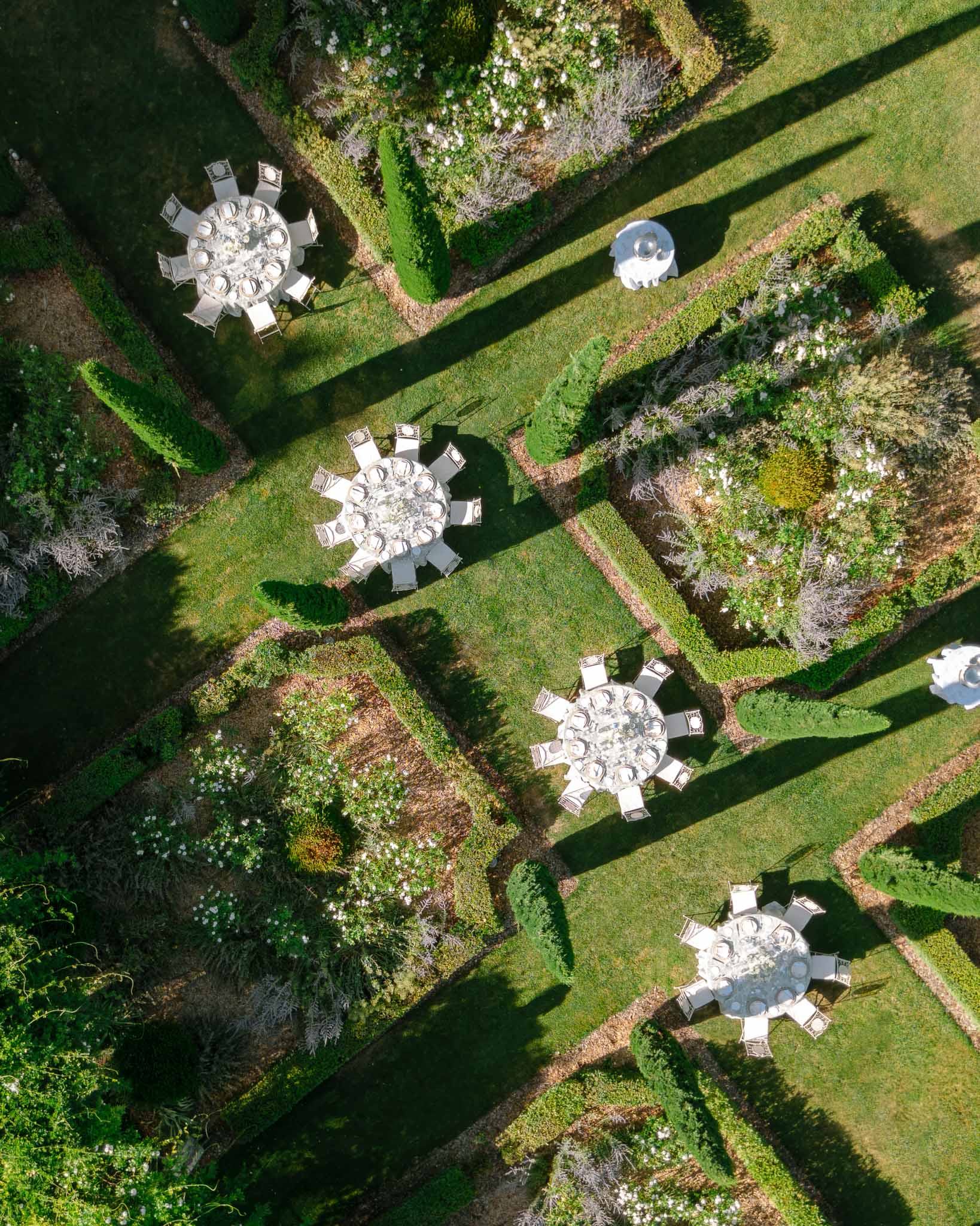 Aerial view of round wedding reception tables set in a formal parterre garden with white decor and box hedging