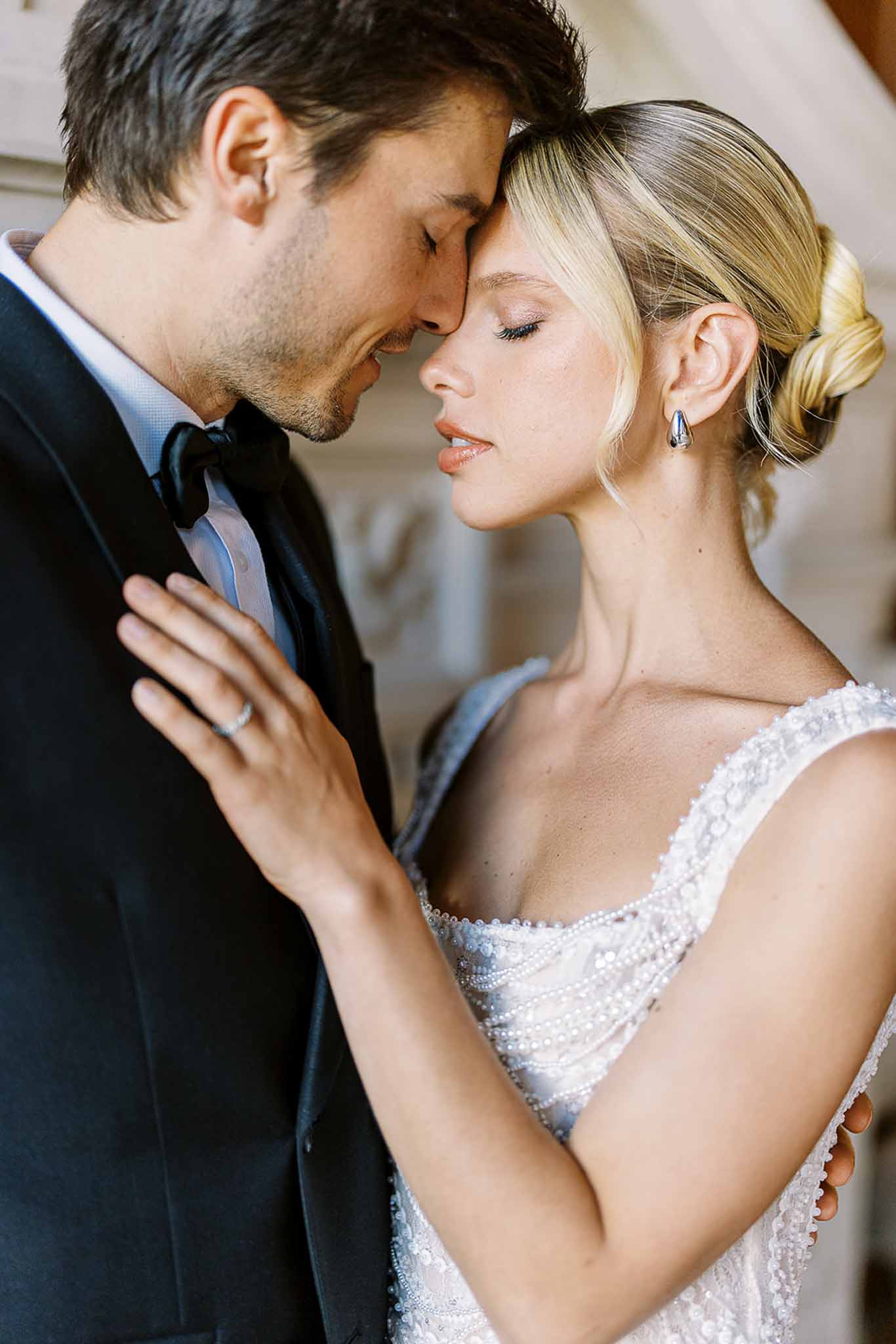 Bride and groom foreheads touching in close-up, bride in beaded pearl gown with silver earrings