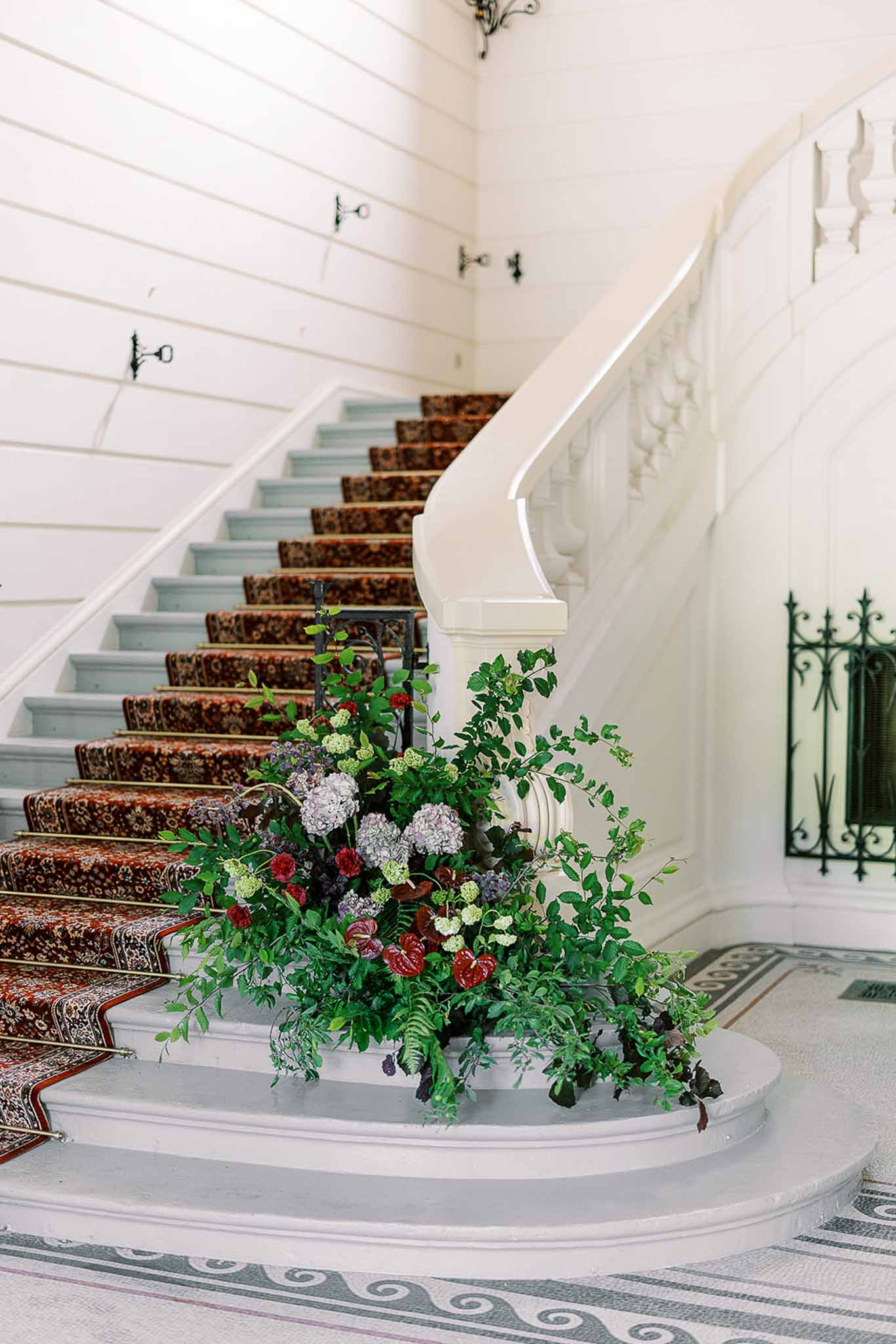 Large floral installation with mauve hydrangeas, burgundy anthuriums, and trailing greenery at base of chateau staircase