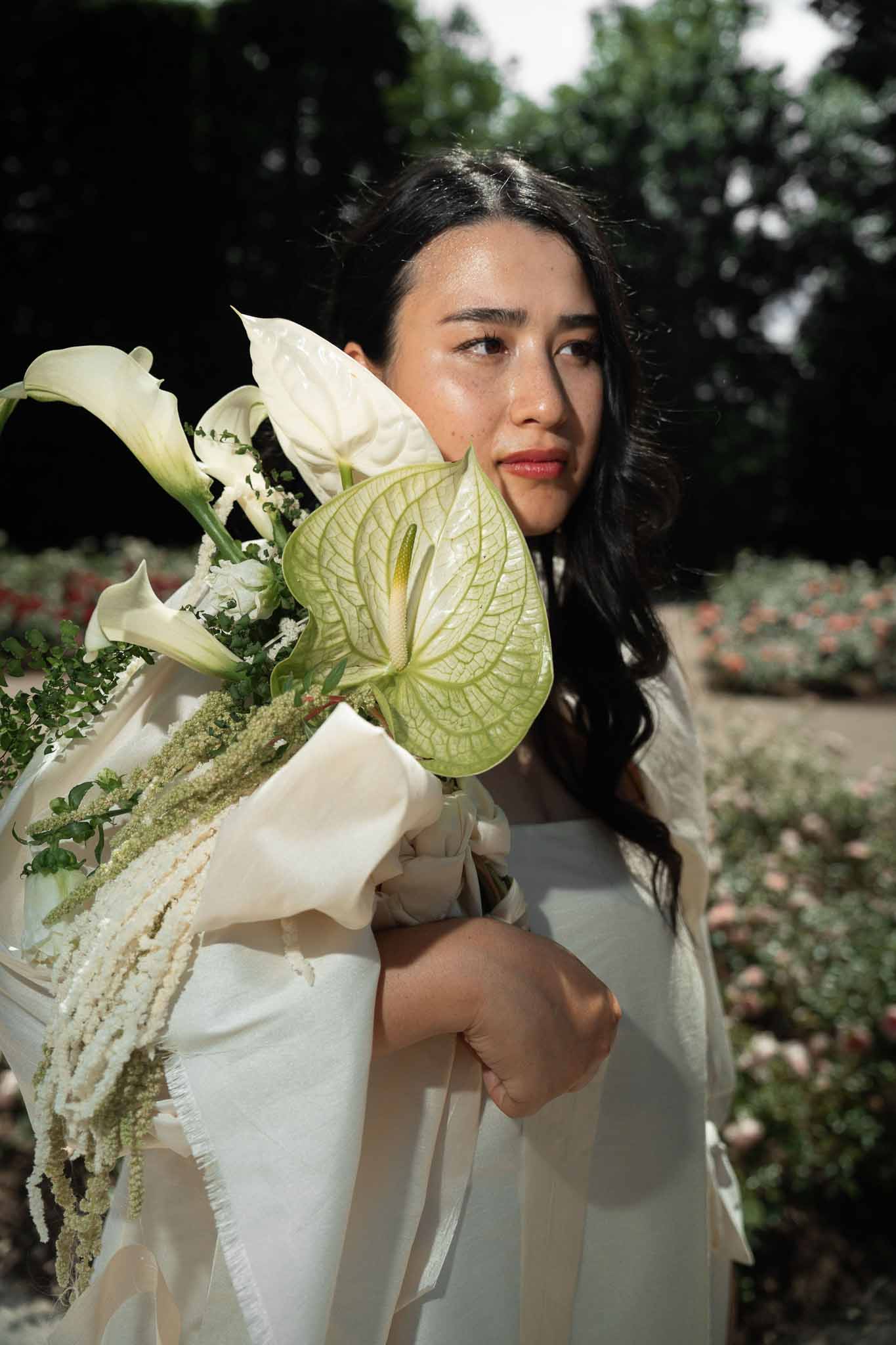 Bride holding modern white calla lily and anthurium bouquet with trailing amaranthus in garden