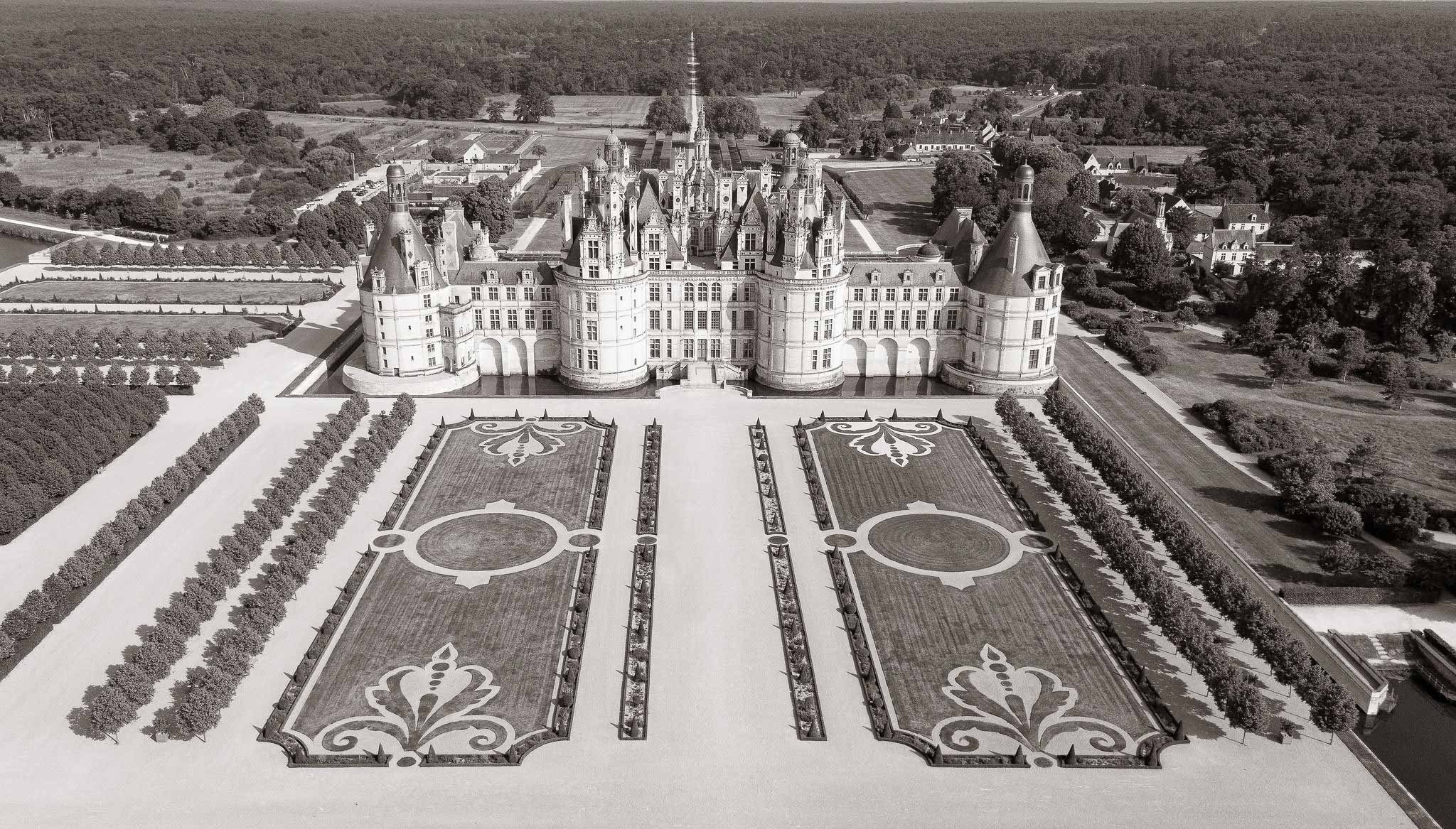 Black-and-white aerial photograph of a Renaissance chateau with formal garden parterres and surrounding woodland