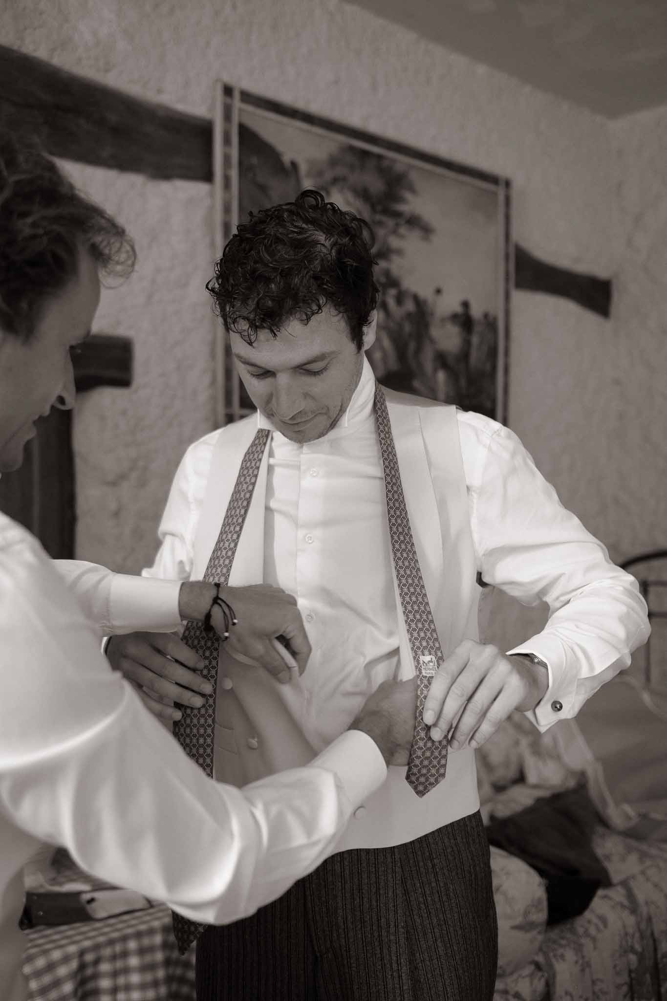 Black and white candid of groom having cufflinks adjusted while wearing patterned suspenders