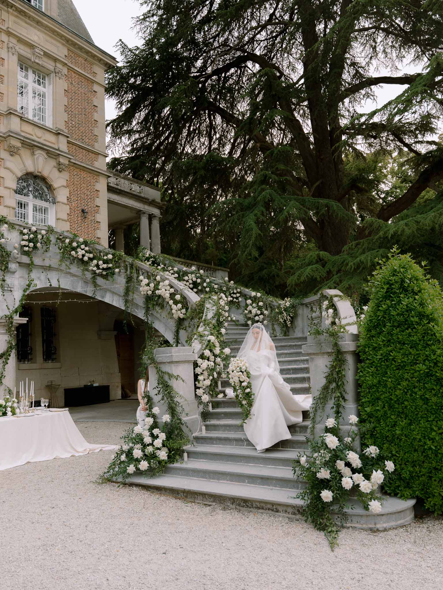 Bride descending chateau stone staircase in ball gown and cathedral veil with cascading white floral installations
