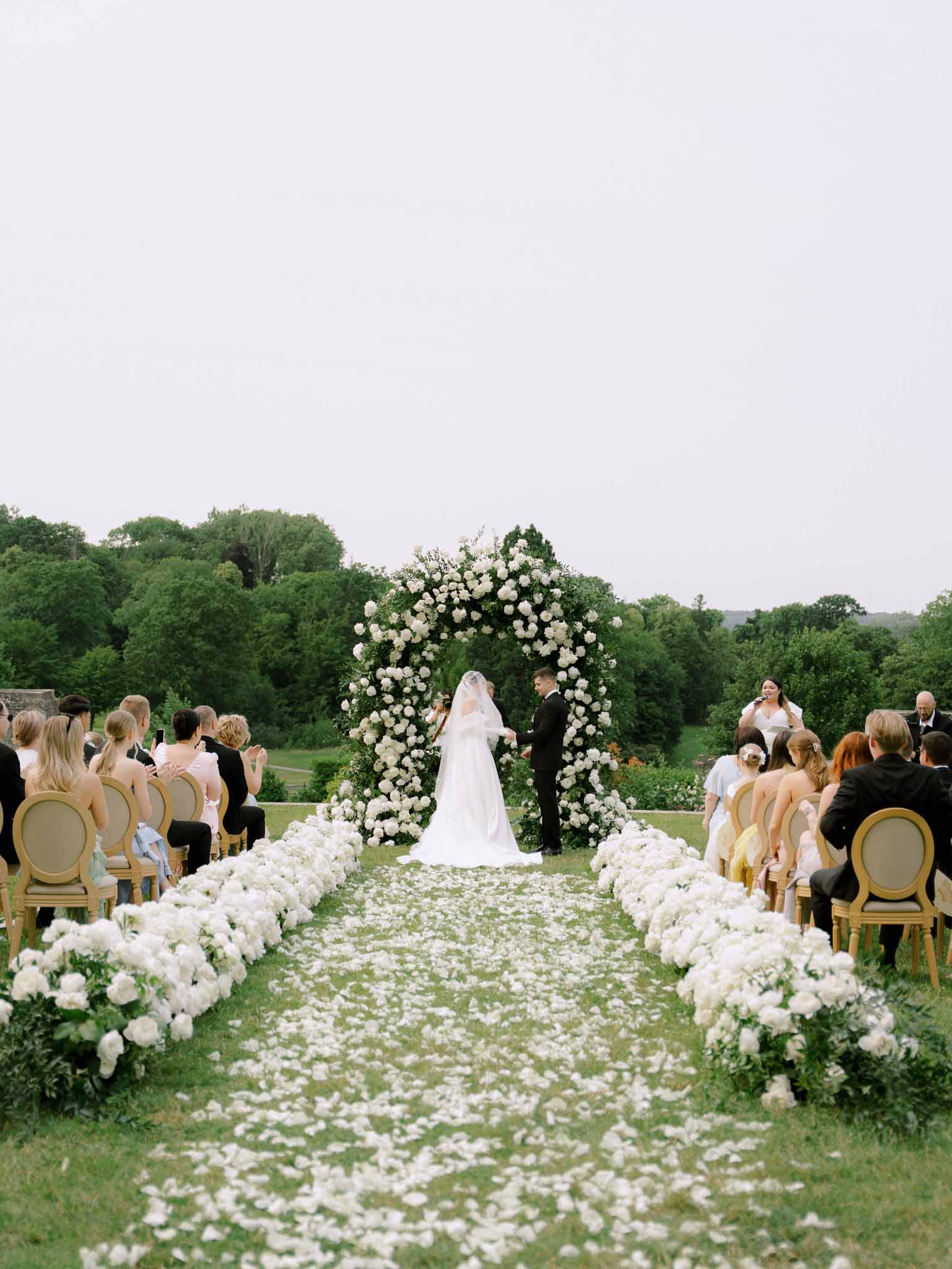50-guest ceremony with white peony aisle rows and circular greenery arch on estate lawn