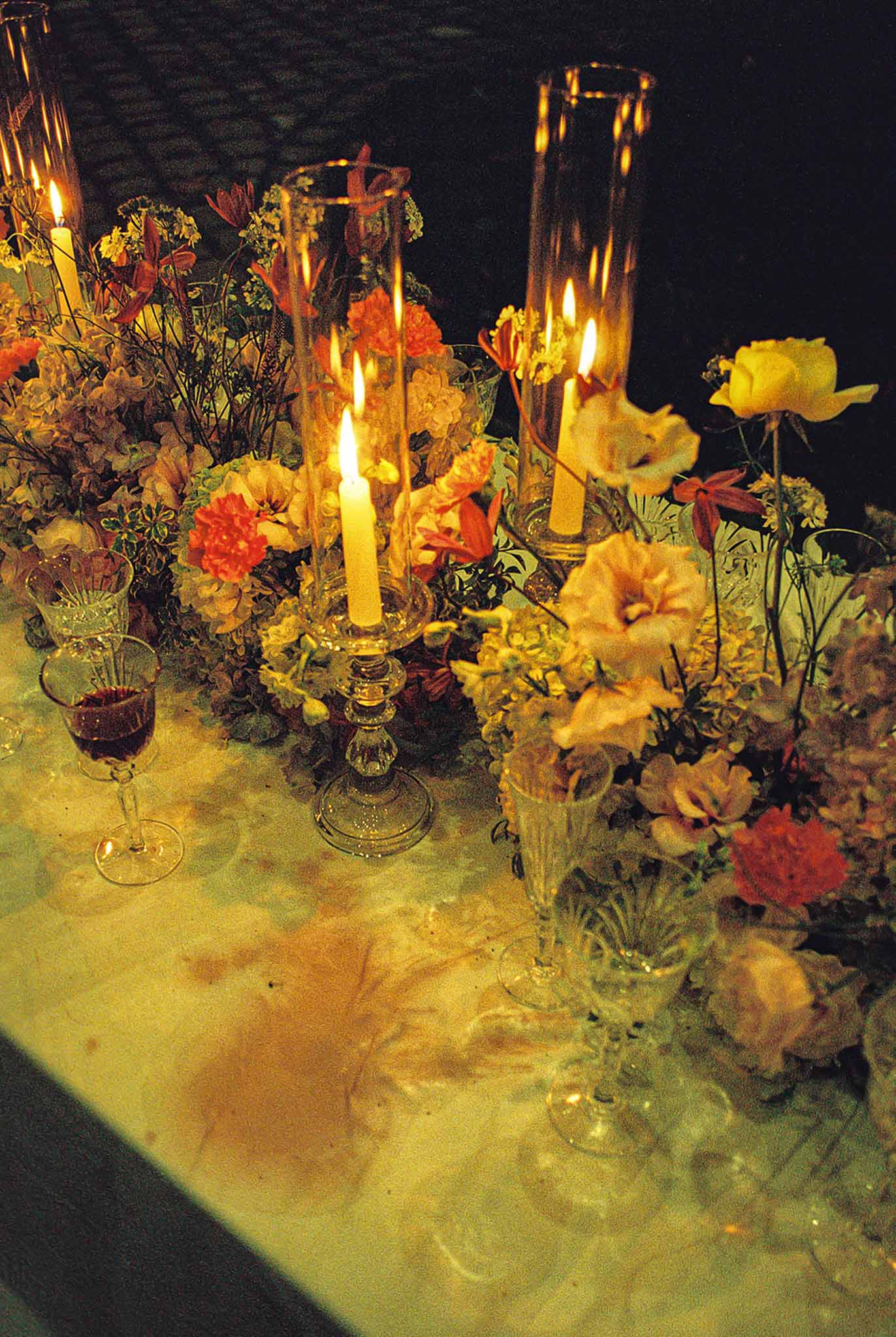Candlelit centrepiece of orange carnations, yellow roses, and dried mauve hydrangea in crystal holders