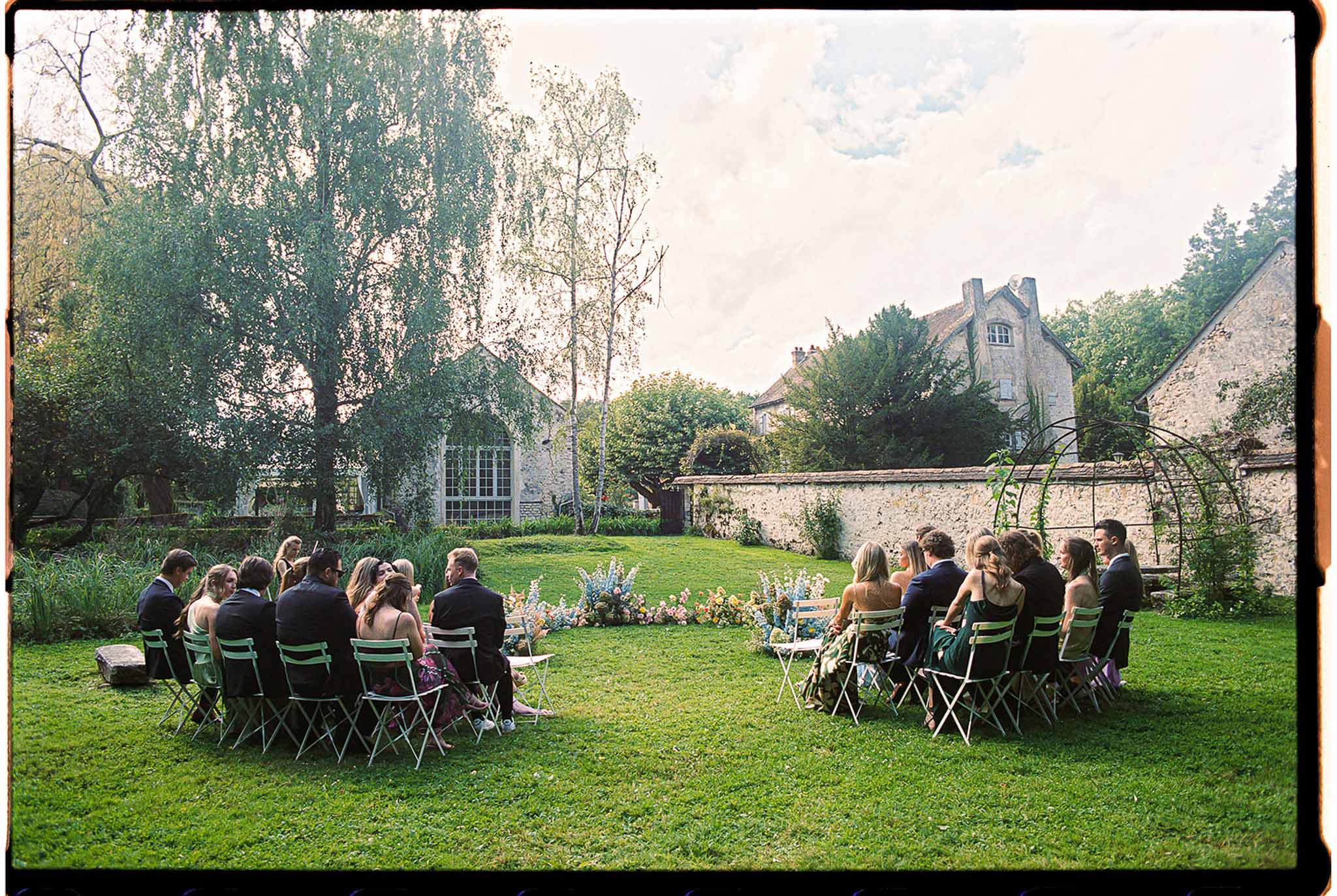 Intimate outdoor ceremony in a walled stone garden with mint green chairs and pastel floral arrangement