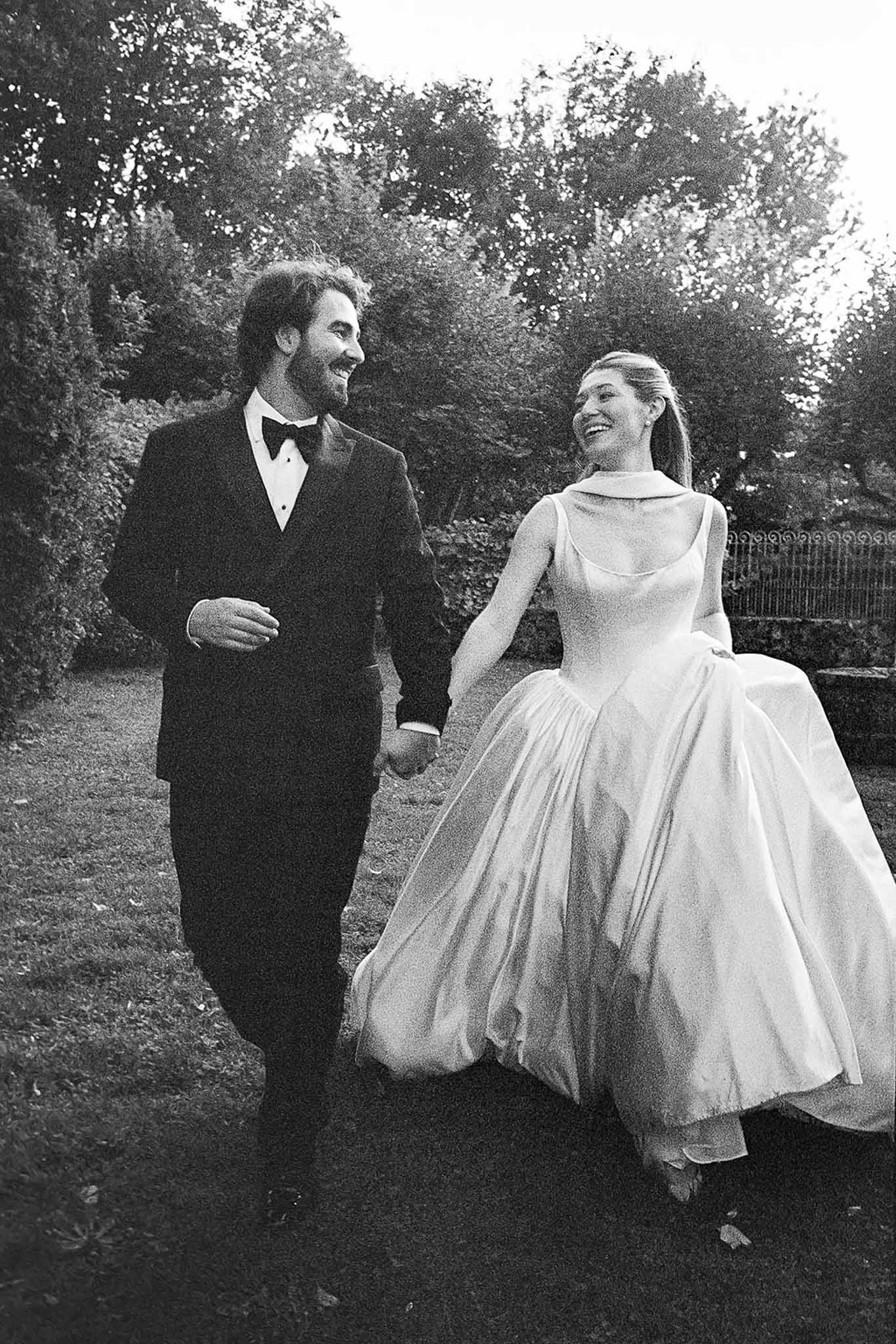 Black and white photo of bride and groom walking hand in hand in a garden
