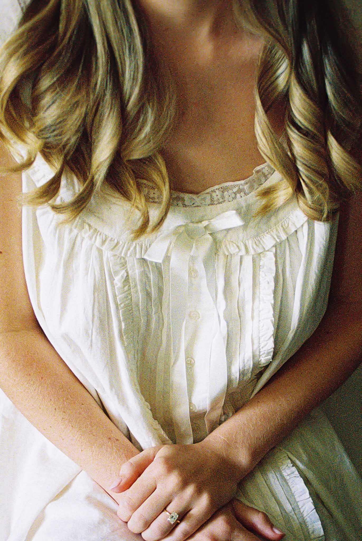Close-up of bride's hands in ivory lace camisole with barrel curls and diamond engagement ring