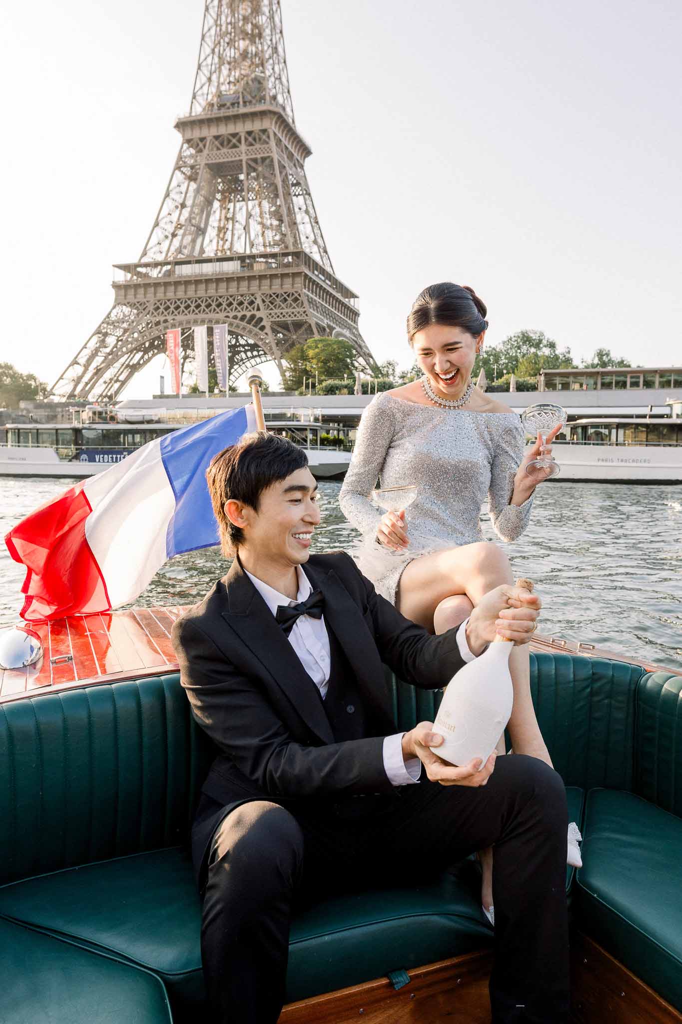 Couple on wooden boat on the Seine popping champagne with Eiffel Tower in background