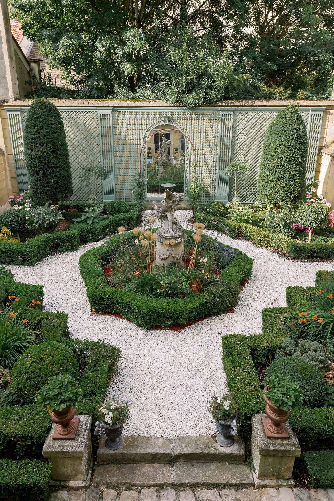 Formal French parterre garden with boxwood hedges gravel paths stone sculpture and conical topiary