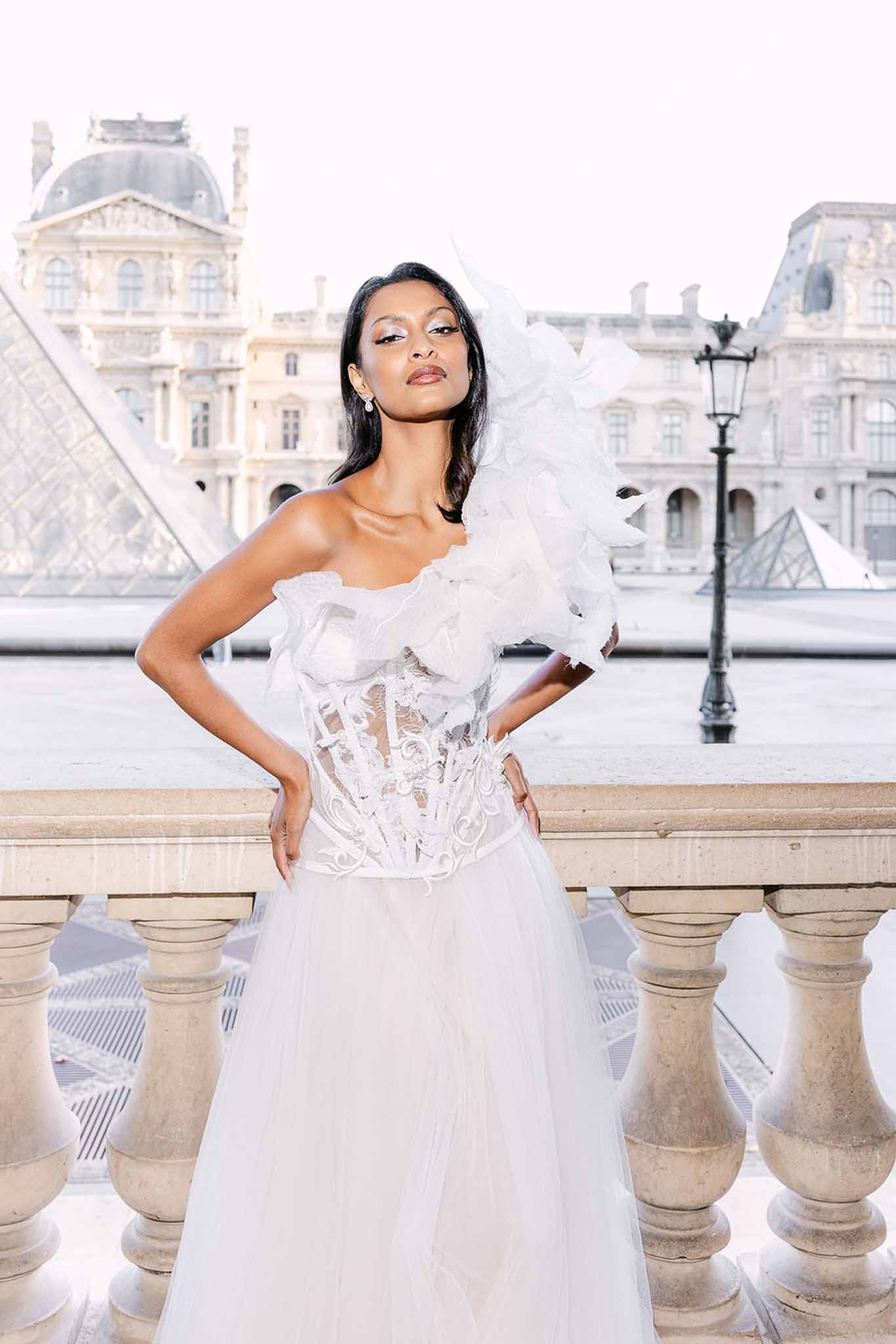 Bride in lace corset gown with ruffled statement sleeve at Louvre pyramid in Paris