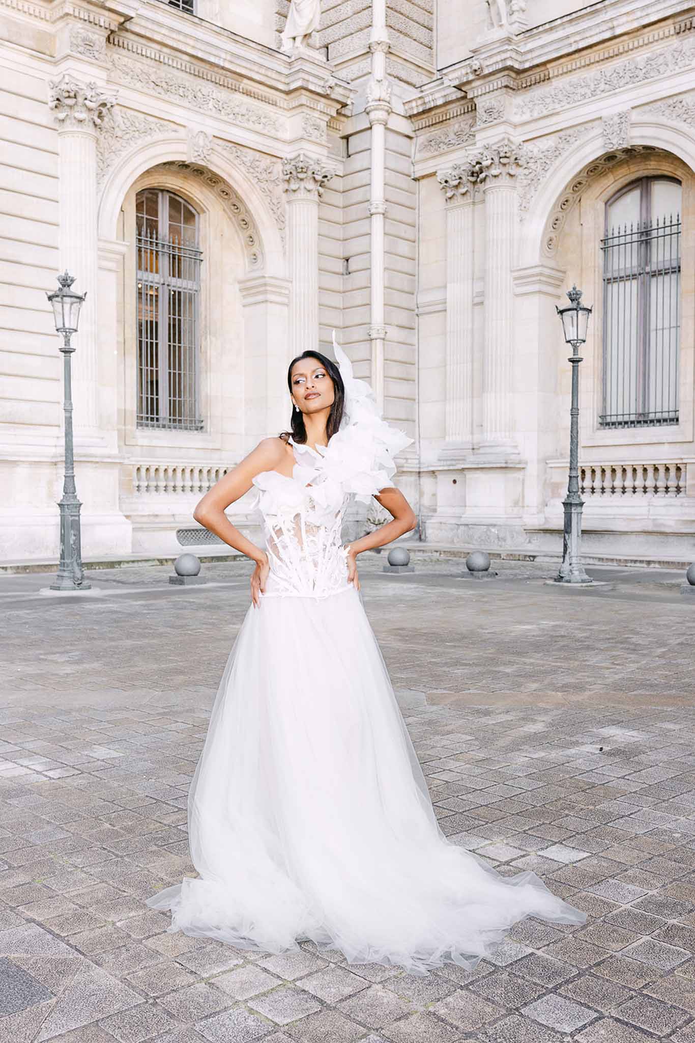 Bride in avant-garde corset gown with ruffle and feather accent posing in Parisian courtyard