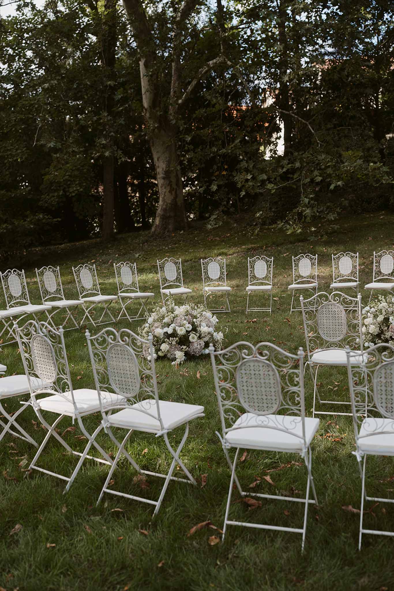 Garden ceremony setup white wrought-iron chairs semicircular layout with white rose and gypsophila aisle arrangements