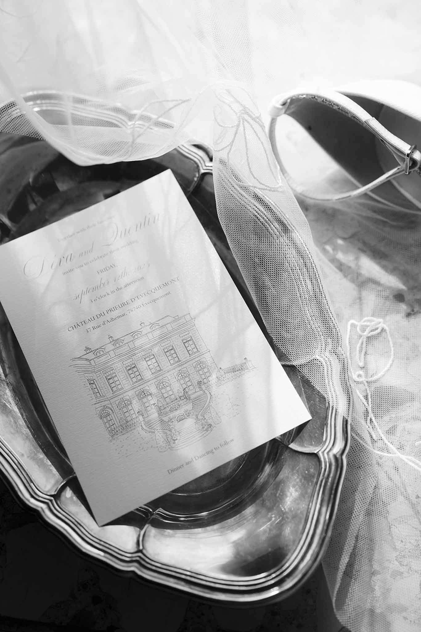Black and white wedding invitation on silver tray with embroidered tulle veil and white bridal shoe