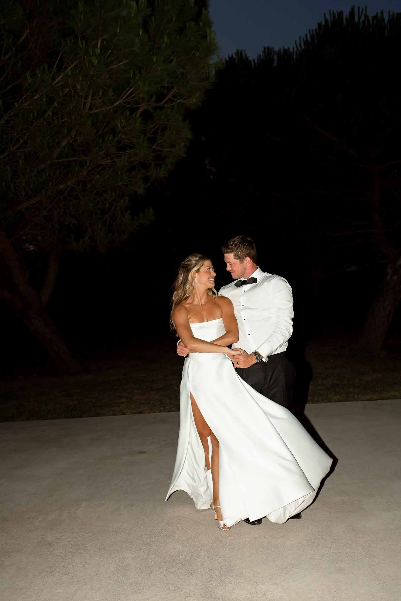 Couple dancing at night on stone surface lit by flash, bride in strapless gown with high slit