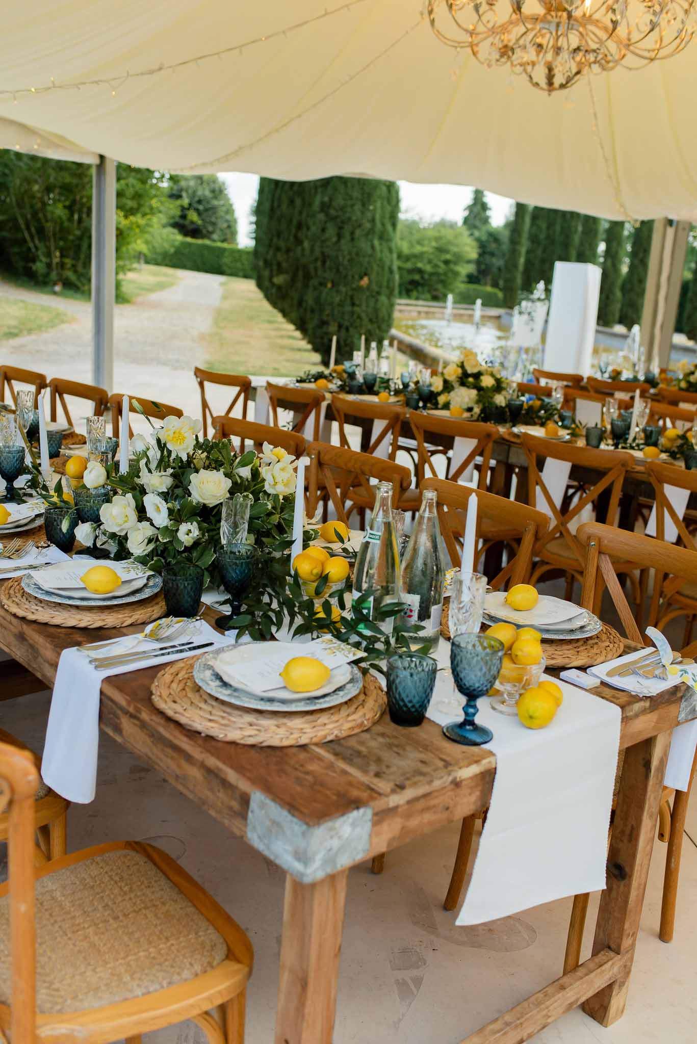 Marquee reception with rustic tables, rattan chargers, green garlands, yellow lemons, and white roses