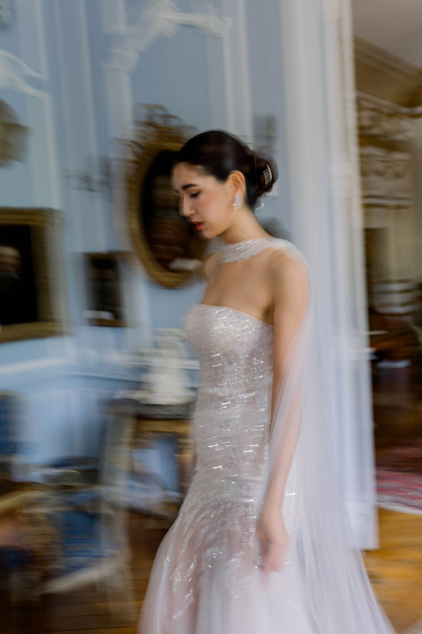 Bride in beaded mermaid gown with billowing veil in blue-panelled chateau salon with gilded mirrors